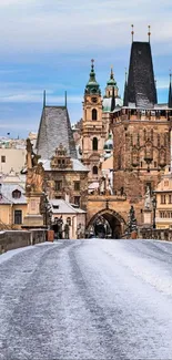 Prague's Charles Bridge blanketed in snow with historic buildings under a blue sky.