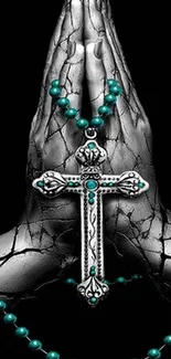 Stone hands with a cross and teal rosary beads on dark background.