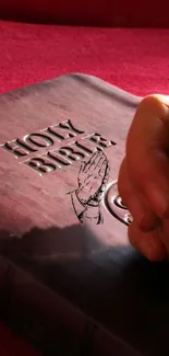 Hands in prayer over Holy Bible with a red background.