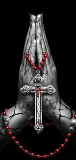 Praying hands with a silver cross and red beads on a dark background.