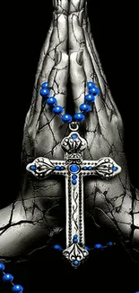 Praying hands with a silver cross and blue rosary beads on a black background.