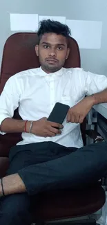 Person in office with mobile phone, seated on a brown chair.