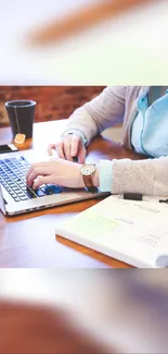 Person typing on a laptop with coffee and notepad in an office setting.