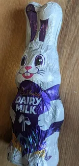 Purple-wrapped chocolate bunny on wooden surface.