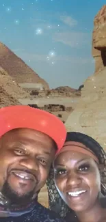 A couple smiling in front of Egyptian pyramids under a starry night sky.