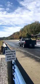 Black truck on race track under blue sky in autumn setting.