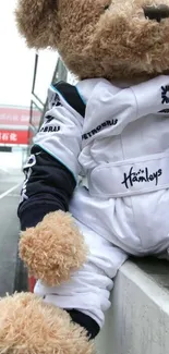 A teddy bear in a racing suit sitting at a racetrack, captured in a mobile wallpaper.