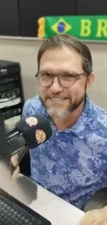 Radio host in studio with Brazilian flag backdrop.