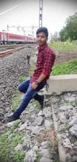 Person in red shirt sitting by train tracks with nature background.