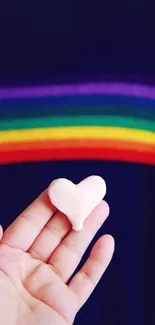 Hand holding heart with rainbow background on wallpaper.