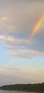 A vibrant rainbow arcs over a peaceful lake under a blue sky.