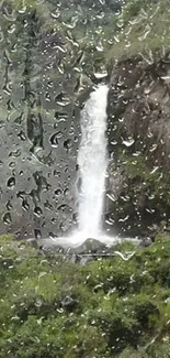 Waterfall seen through raindrop-covered glass, lush greenery surrounds the scene.