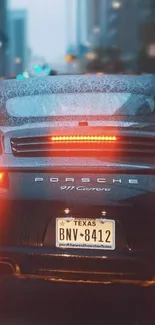 Porsche 911 Carrera driving in rainy cityscape with lights aglow.