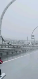 Motorcycle riding on a rainy day across an urban bridge.