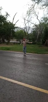 Person stands on a rainy road surrounded by lush green trees.