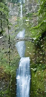 Waterfall with raindrops on glass and lush greenery.