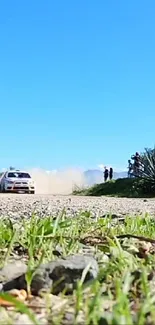 Rally car speeding on a scenic dirt road under a blue sky.