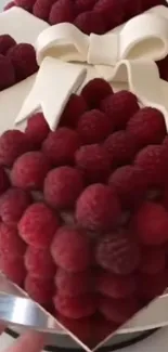 Heart-shaped cake with raspberries and white bow.