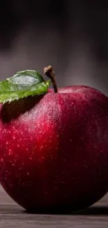 Vibrant red apple on a wooden table with a dark background.