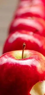 A row of vibrant red apples with one bitten on wooden surface.