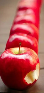 Row of red apples with one bitten in vibrant mobile wallpaper.