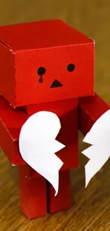 Red cardboard robot holding broken heart.