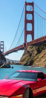 Red sports car parked under the Golden Gate Bridge on a clear day.