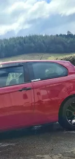 Red car parked near lush green hills under a blue sky.