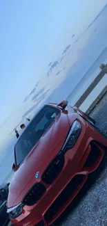 Red car parked by the ocean under a clear sky at sunset.