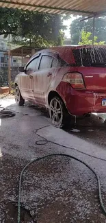 Red car undergoing a wash with foam and sunlight.