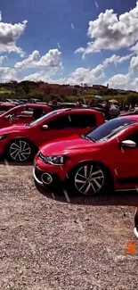 Bright red cars lined up under a clear blue sky at an outdoor event.