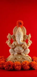 Ganesha idol with orange flowers on a red background.