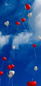 Red and white heart balloons floating in a bright blue sky.