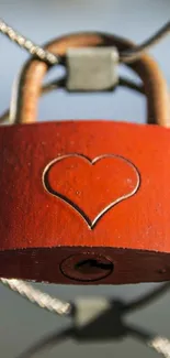 A red padlock with a heart symbol hanging on a fence.