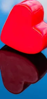 Vibrant red heart with reflection on blue sky background.