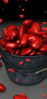 Overflowing bucket of red hearts on dark background.