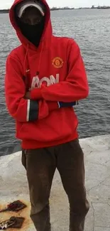 Person in red hoodie standing by the ocean shore.