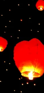 Floating red lanterns in night sky on a dark background, glowing brightly.