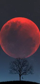 Silhouette tree against a red moon backdrop in a starry night sky.