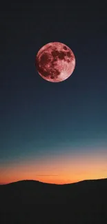 Red moon in a twilight sky over a dark silhouette landscape.