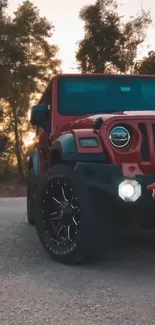 Red Jeep parked on a scenic road at sunset with trees in the background.