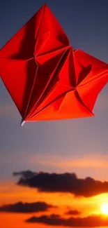 Red origami kite flying against a sunset sky.