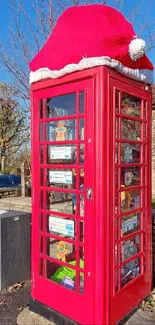 Festive red phone booth with Santa hat in sunny setting.