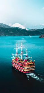 Majestic red ship sailing on turquoise waters with mountain backdrop.