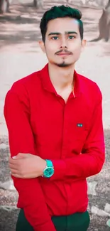 Young man in red shirt standing outdoors with a blurred natural background.