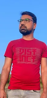 Man in red shirt standing under blue sky, creating a vibrant wallpaper background.