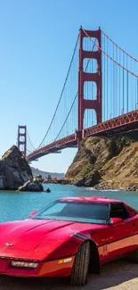 Red sports car by a famous bridge under clear blue skies.