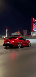 Red sports car driving through neon-lit city streets at night.