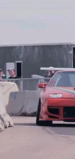 Red sports car racing around a track with barriers.