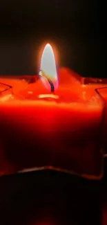 Star-shaped red candle with a glowing flame in a dark setting.